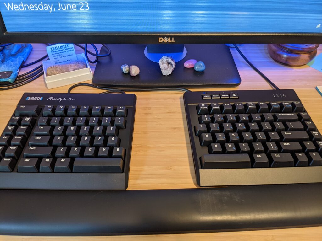 Split Keyboard in front of computer screen, shiny rocks arrayed under monitor 