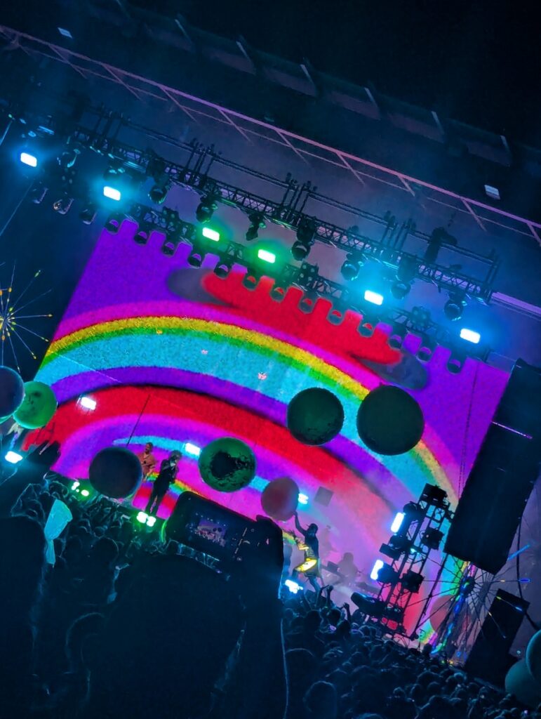 Several balloons floating above the crowd at a Flaming Lips show in the background, foreground is someone else's camera getting in the way of mine